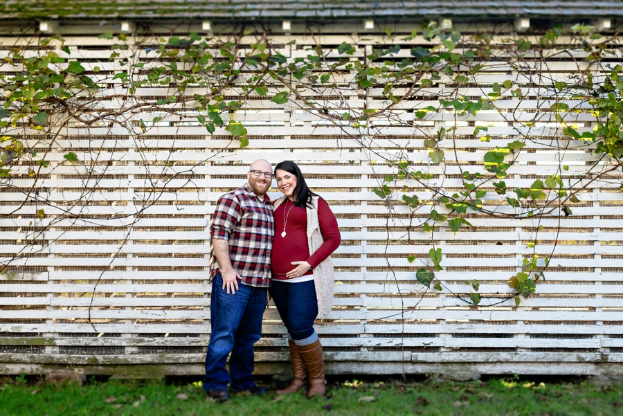 A pregnant couple stand in front of a wood building for their maternity session in valley forge state park.